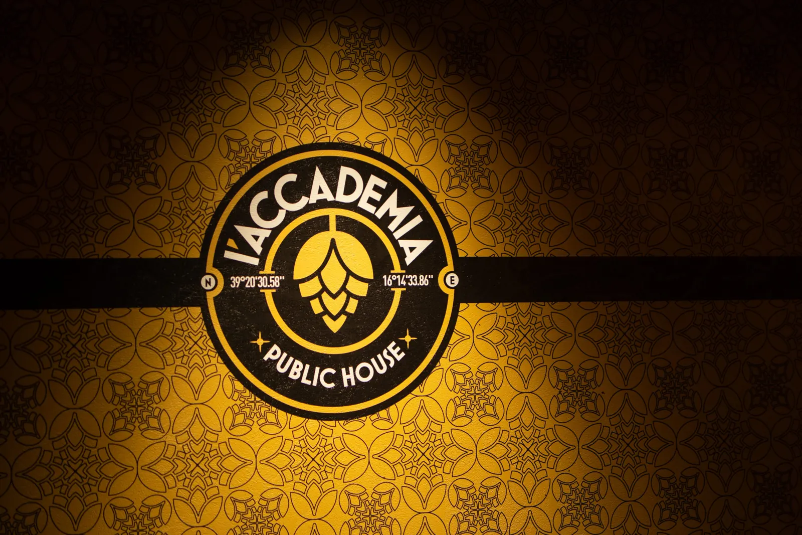 Il logo dorato de L’Accademia sulla parete decorata con motivi di luppolo